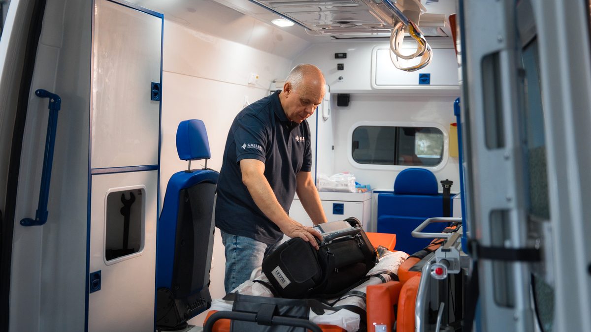 Ralf Gäbler arbeitet im Innenraum eines Rettungswagens an einem Notfallrucksack, daneben Trage und Halterungen